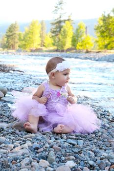 Beautiful brunette baby girl sitting on pebble beach