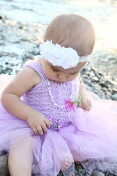 Beautiful brunette baby girl sitting on pebble beach