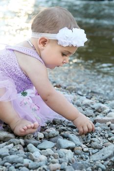 Beautiful brunette baby girl sitting on pebble beach