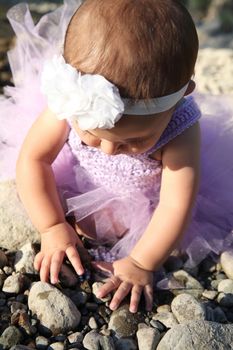 Beautiful brunette baby girl sitting on pebble beach