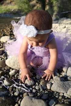 Beautiful brunette baby girl sitting on pebble beach