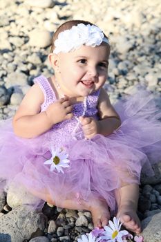 Beautiful brunette baby girl sitting on pebble beach