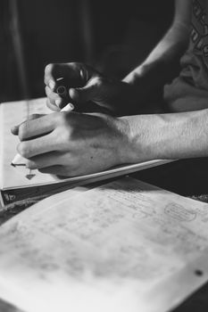 Black and white close-up of the hands of a teenage student doing his homework assignment, consisting of solving a mathematical exercise or problem, with intellectual effort, by writing, on paper