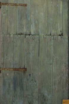 An old green painted wooden door with woodworm holes and rusty hinges