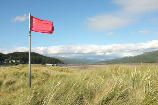 A red warning flag on a post on a sand dune over looking an estuary.