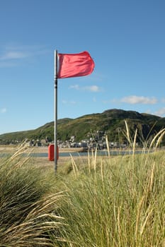A red flag flutters in the wind over looking an estuary with a town in the distance.