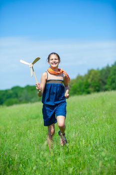 Cute girl runing on grass in summer day holds wooden windmill in hand