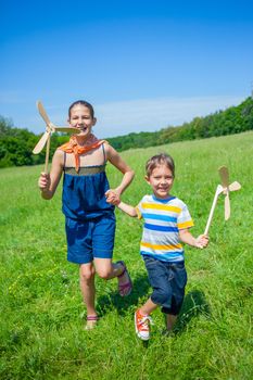 Cute kids runing on grass in summer day holds wooden windmill in hand