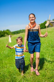 Cute kids runing on grass in summer day holds wooden windmill in hand