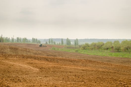 wide big brown plowed field in rural image with tractor in the distance