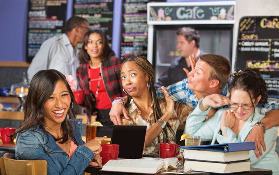 Student laughing at friends reaction to kissing man in cafe