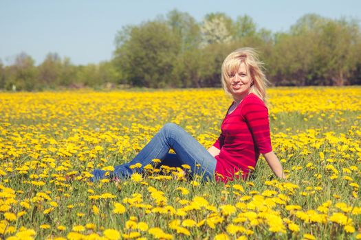 smiling woman sitting in field of dandelions