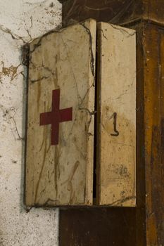 An old first aid kit on a dirty and rusty wall covered by cobwebs