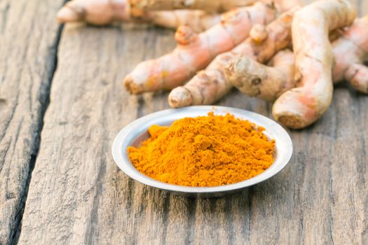 Fresh turmeric root, and turmeric powder on wood background- shallow depth of field 