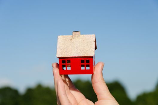 woman hand hold small metallic house miniature on blue sky background
