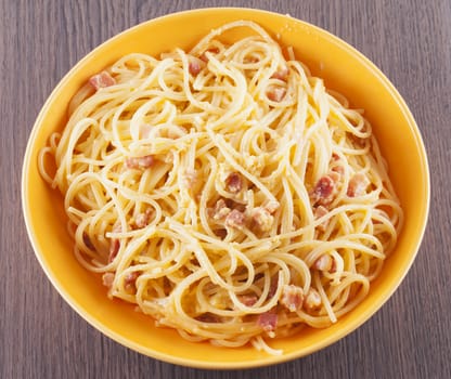 Spaghetti alla carbonara in yellow plate, wooden table