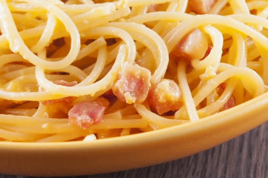 Spaghetti alla carbonara in yellow plate, wooden table