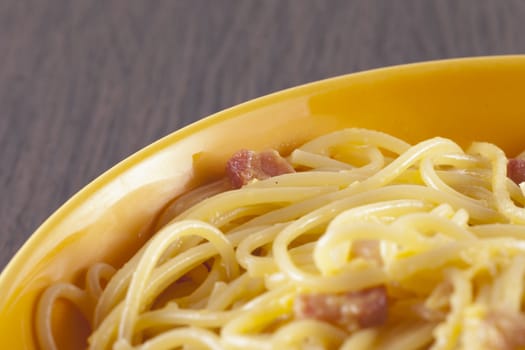 Spaghetti alla carbonara in yellow plate, wooden table