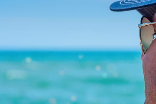 Unshaven man in sunglasses looking at sea, shallow depth of field of the sea