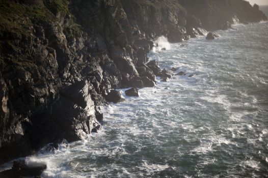 stormy seas crashing into a jagged rocky coastline on the south coast of cornwall, england