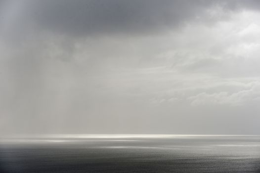 Calm seascape with stormy sky where sun-rays get through the clouds. 