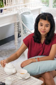 Pretty woman pouring tea from the teapot into a white ceramic cup 