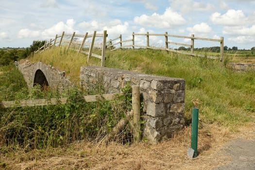 An old stone bridge overgrown with grass with a rickety wooden fence.