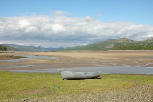 A grey painted boat on the bank overlooking an estuary with the tide out.