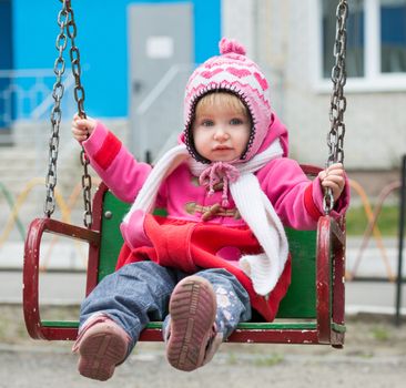 Little girl on the playground ride on a swing