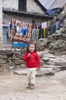 Small girl armed with a toy gun standing by a large stone inscribed with Buddhist text on the path to Everest Base Camp in the Himalaya Mountains, Nepal