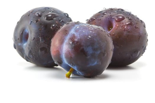 Three plums with drops of water on a white background