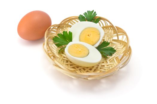 one egg, two halves of boiled eggs and parsley leaves in a straw plate