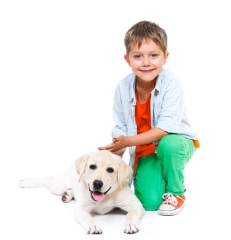Cute little boy kneeling with his puppy labrador smiling at camera on white background