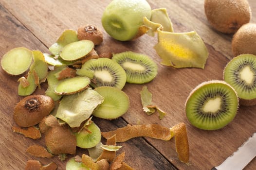 Preparing a tropical kiwifruit dessert with a high angle view of peels, peeled kiwi fruit and sliced fruit being prepared in a rustic country kitchen