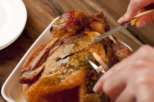 Close up view of the hands and utensils from above of a man carving a delicious brown roast chicken for dinner