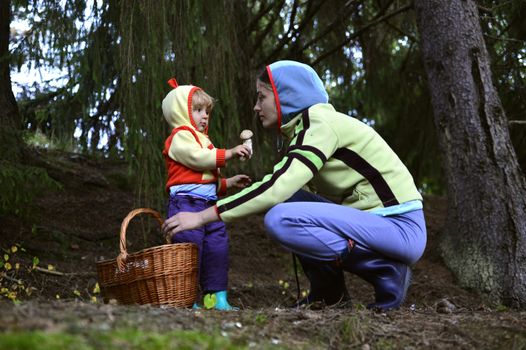 A mother and her little girl picking mushrooms in the forest in the bascket, showing  ones