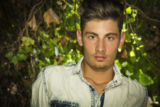 Handsome young man looking at camera. Plants and bushes around him