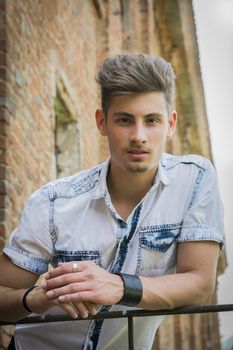 Handsome young man outdoors leaning on hand-rail, looking down at camera