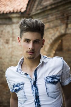 Handsome young man outdoors in front of old house or palace, looking at camera
