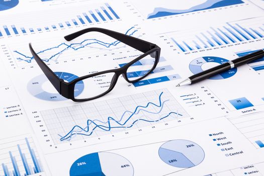 glasses and pen on blue charts, graphs, data and document background for financial and business concepts