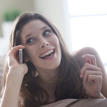 Happy young woman talking on the phone while in bed 