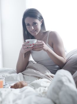 Lovely young woman lying with a cup of coffee and a tray of breakfast 