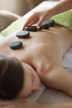 Young woman receiving a hot stone massage therapy at spa.