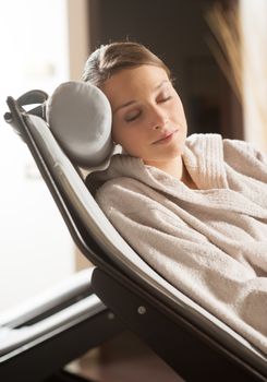Woman in bathrobe relaxing at spa with eyes closed.