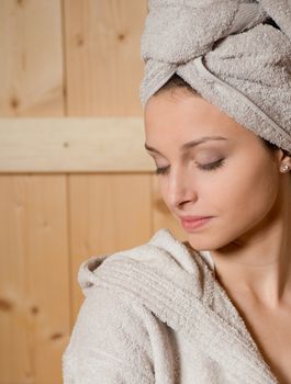 Young woman relaxing in sauna lying on a bench with eyes closed.