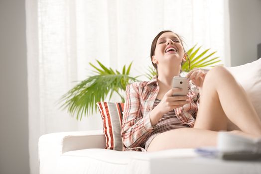 Girl using mobile phone and lying on sofa in the living room.
