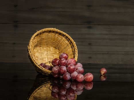 red grapes served in basket on black glass and on wood background