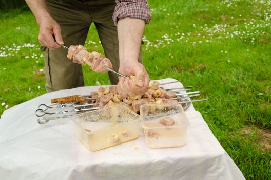 man put neatly skewer green pork meat prepared for cooking on a campfire