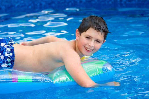 Happy young boy with inflatable water lounger in the swimming pool