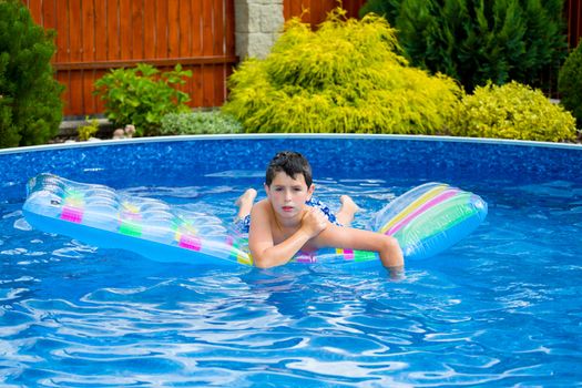 Happy young boy with inflatable water lounger in the swimming pool